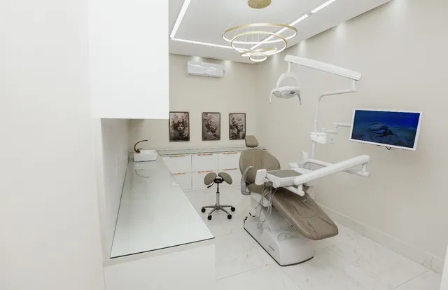 Consultório odontológico branco, com cadeira e monitor, na Clínica Sabbin