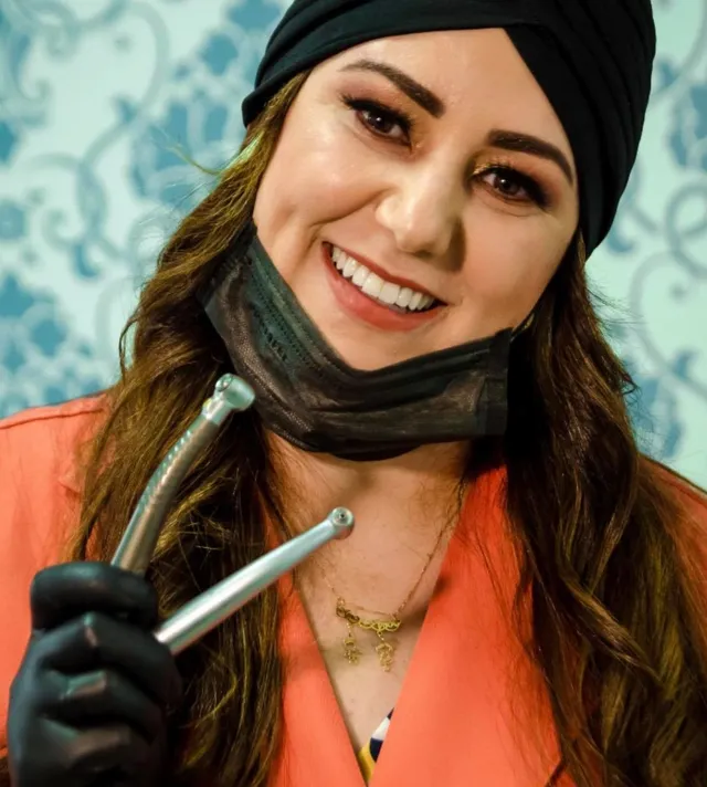 Dra. Wânia Veloso sorrindo, de luvas, segurando uma caneta odontológica