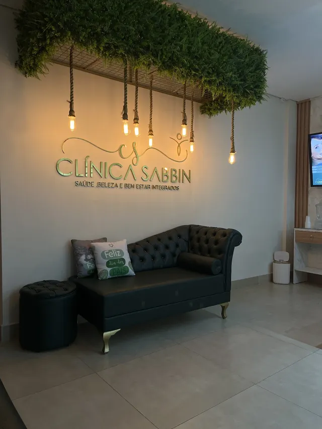 Recepção da Clínica Sabbin com o letreiro na parede de plantas e luminárias pendentes